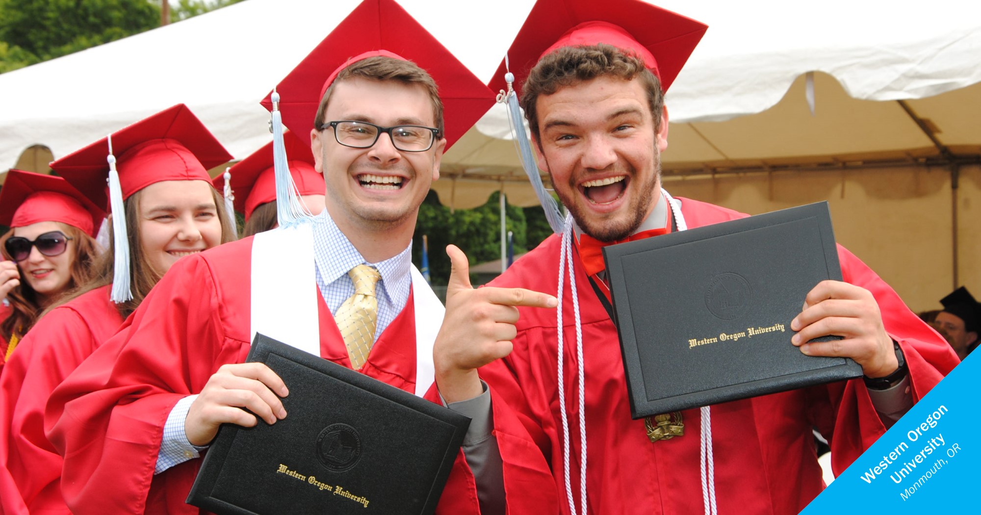 Western Oregon University graduates smiling and pointing to diplomas