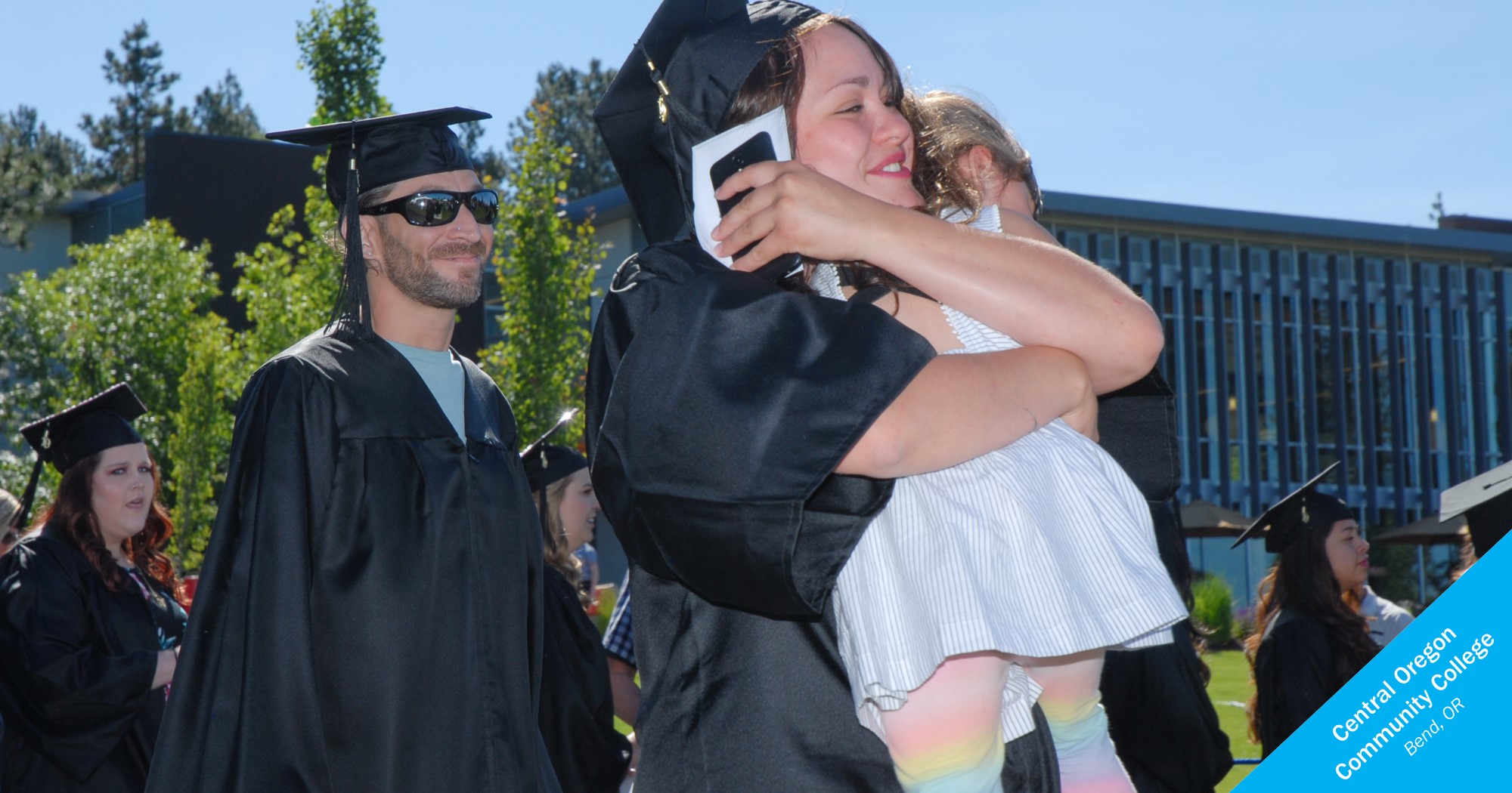 Central Oregon Community College female graduate hugging a child 